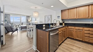 A modern kitchen with wooden cabinets, a black countertop, and a built-in dishwasher. - Guest Favorite ~ Newly Renovated ~ 18th Floor Direct Ocean + SkyWheel Views (Myrtle Beach)