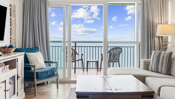 A room with a sofa, a chair, a coffee table, a TV, and a balcony with a view of the sky and clouds. - Guest Favorite ~ Newly Renovated ~ 18th Floor Direct Ocean + SkyWheel Views (Myrtle Beach)