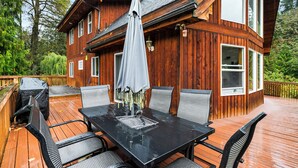 Eine Holzterrasse mit einem schwarzen Tisch und Stühlen, einem überdachten Grill und einem großen Sonnenschirm.