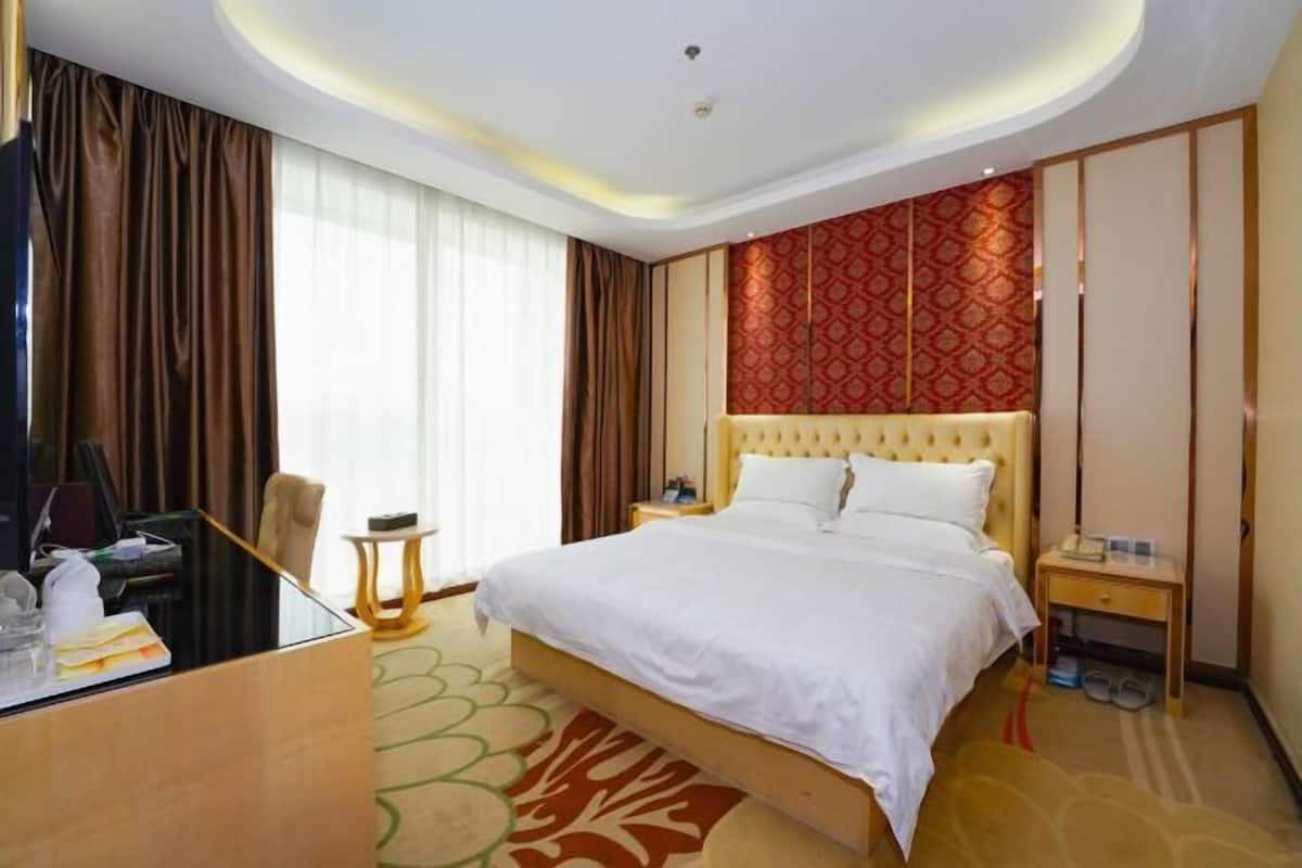 Quarto de hotel com cama grande, escrivaninha, cadeira, televisão e janela com cortinas.