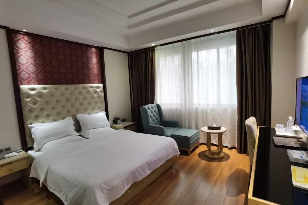 Quarto de hotel com uma cama grande, uma escrivaninha com computador, uma cadeira e uma mesa redonda pequena.