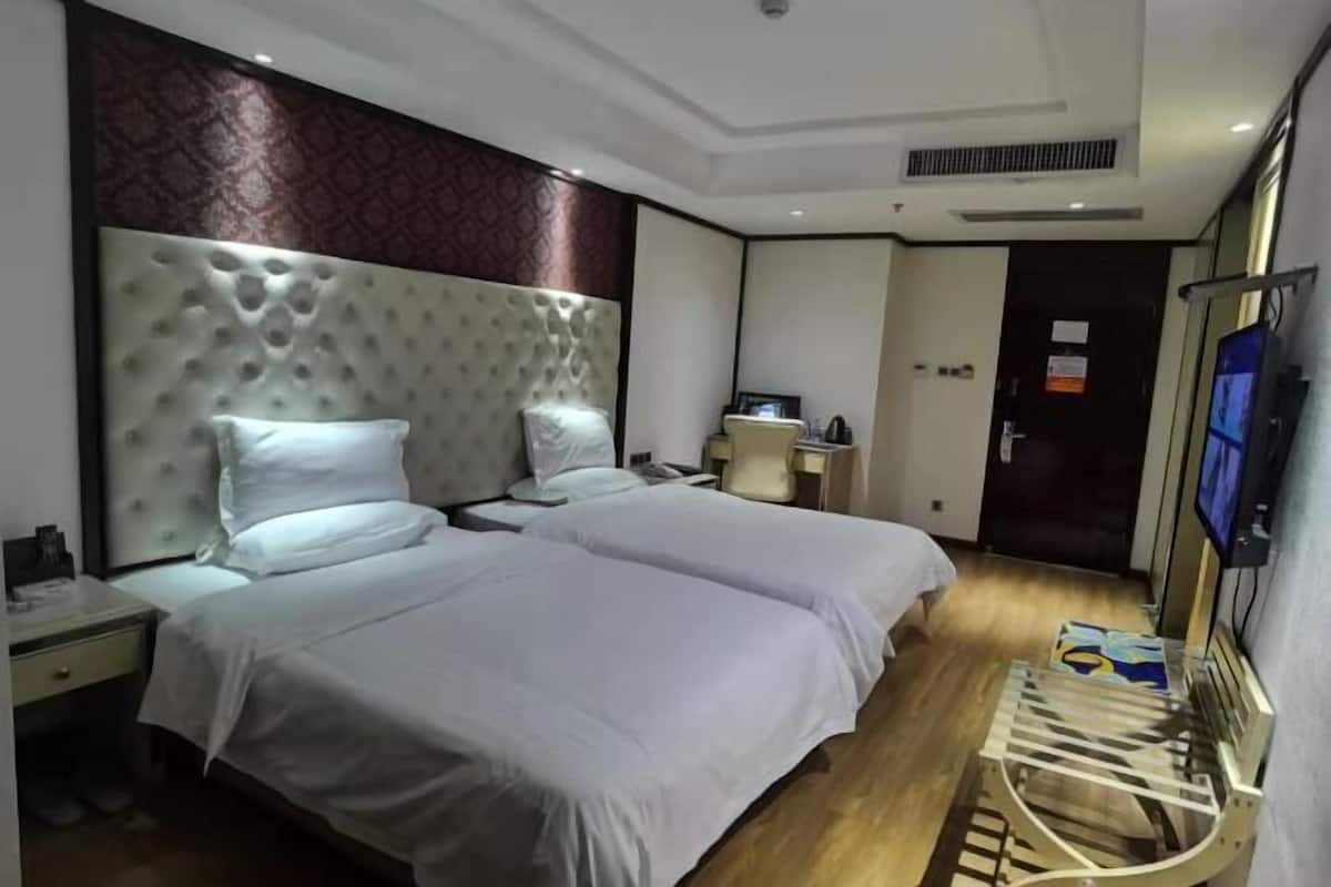 Quarto de hotel com duas camas, piso de madeira, cabeceira grande, escrivaninha com cadeira e televisão.