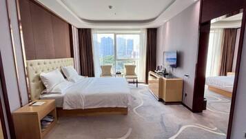 Habitación de hotel con una cama grande, un escritorio con silla, televisión y vista a la ciudad.