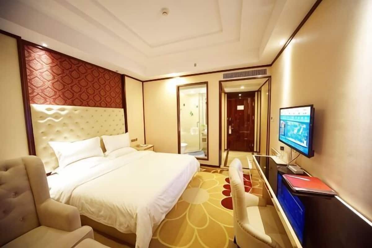 Quarto de hotel com cama, escrivaninha, cadeira, televisão e espelho.