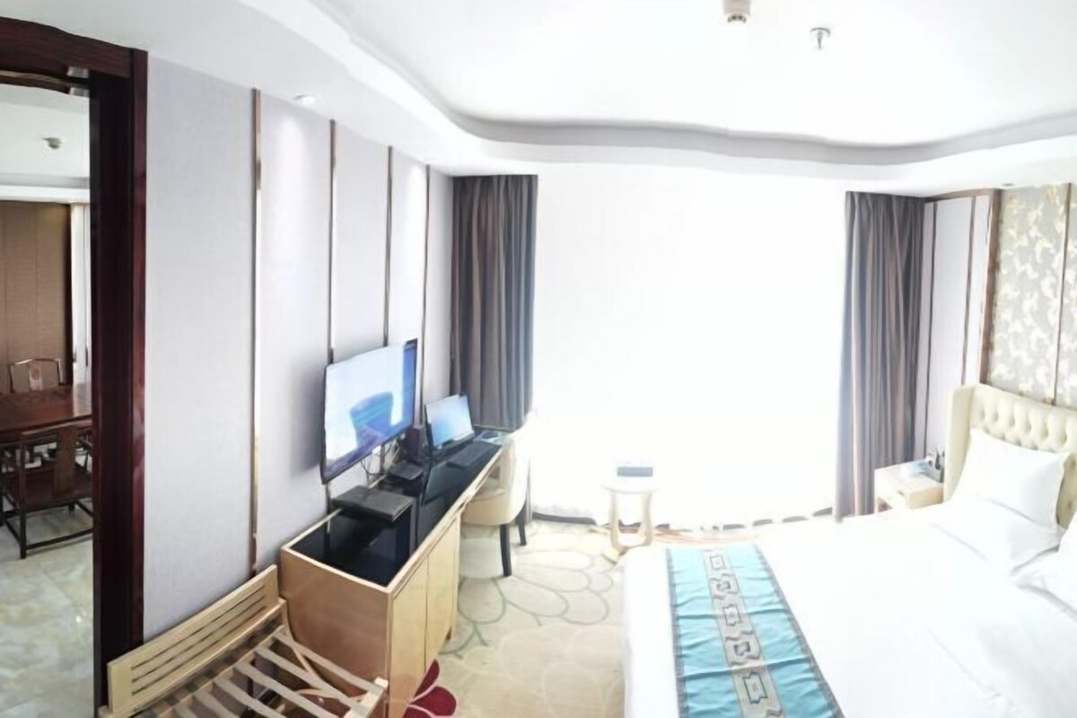 A hotel room with a bed, a desk with a computer, a television, and a wardrobe.