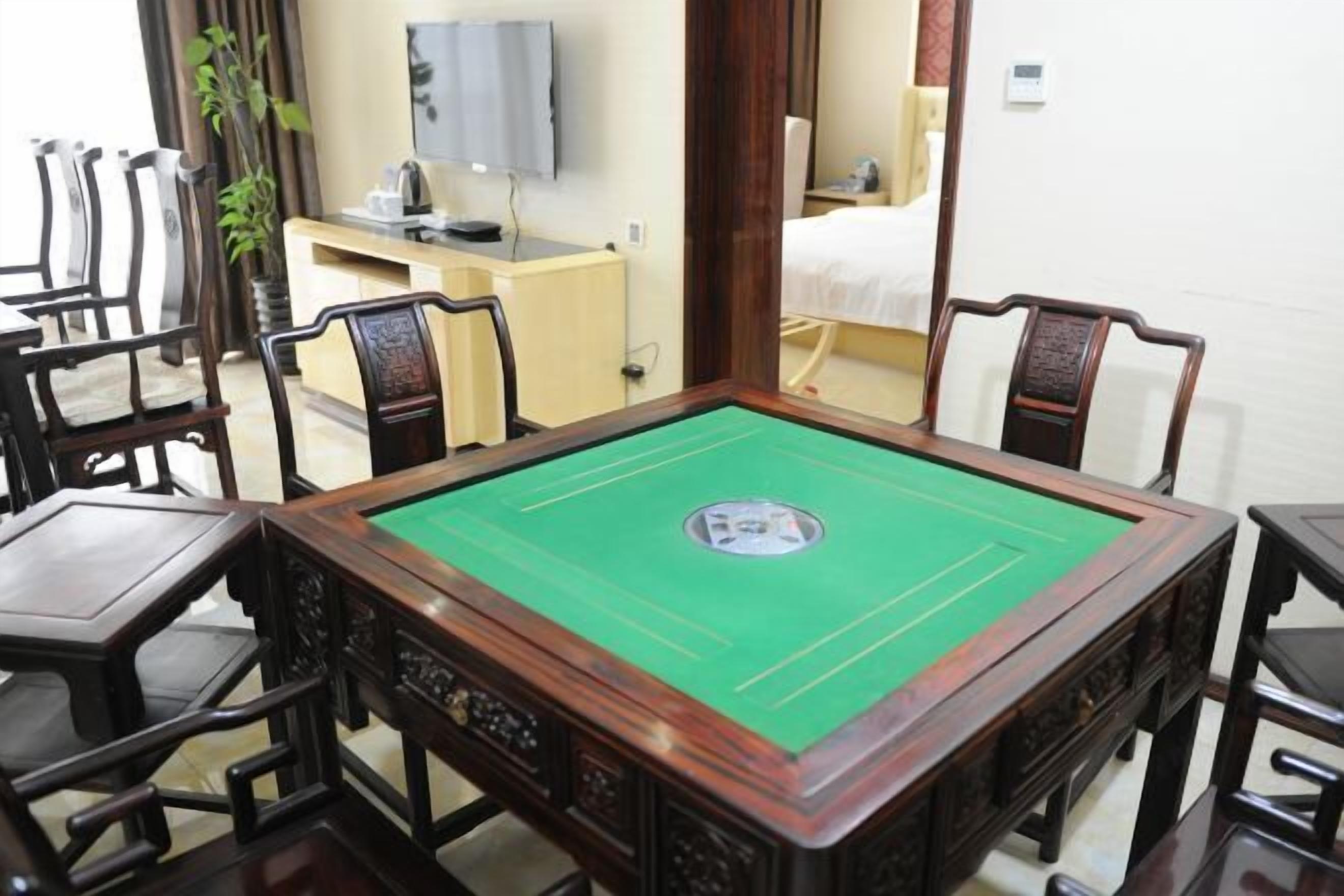 A pool table with surrounding wooden chairs, a television mounted on the wall, and a bed in the background.