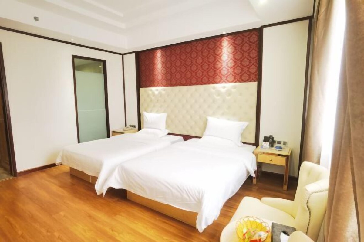A hotel room with a double bed, a bedside table, a chair, and a red patterned headboard.