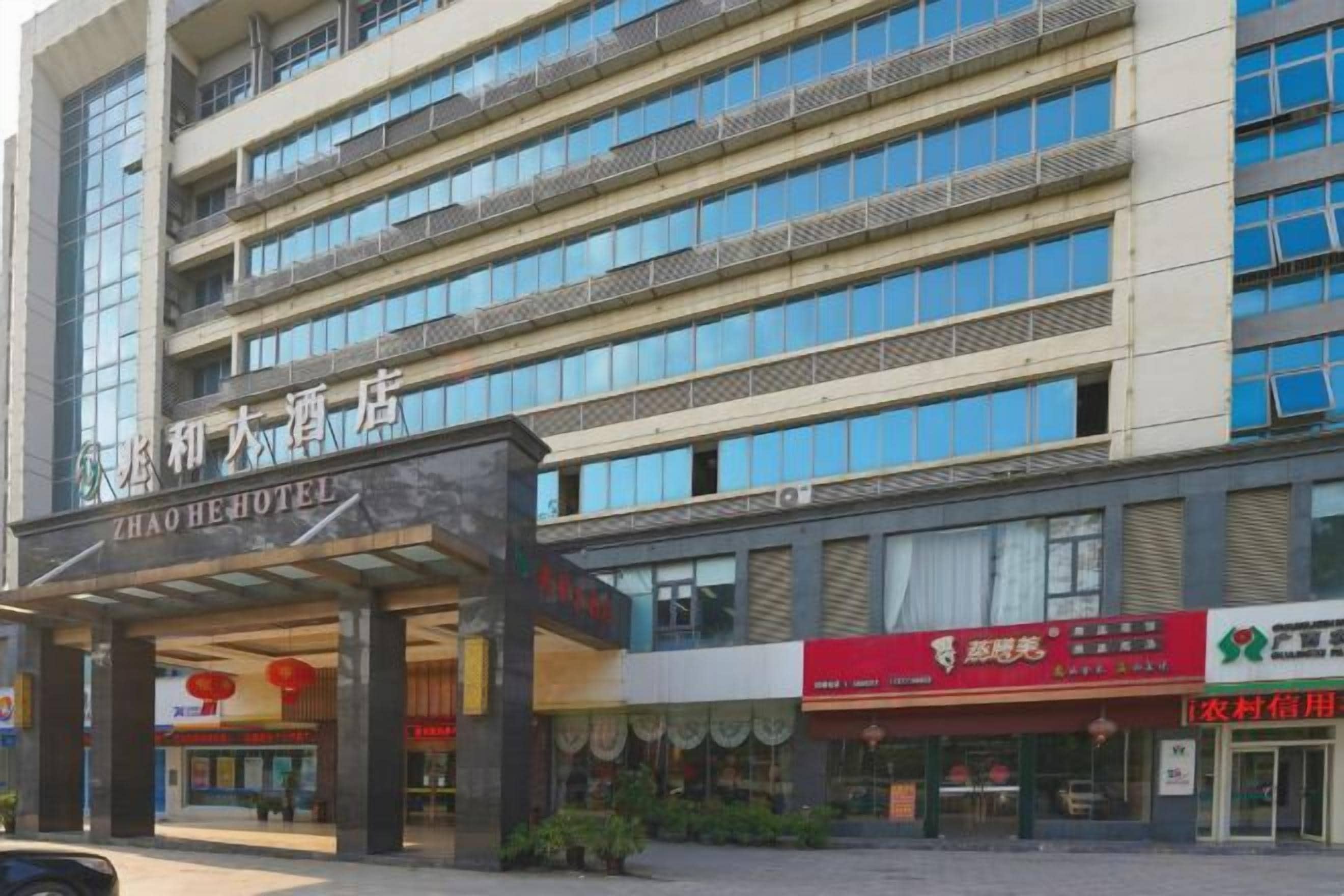 Un hotel de varios pisos con una entrada destacada, señalización para diferentes negocios y una vista clara de la fachada del edificio.