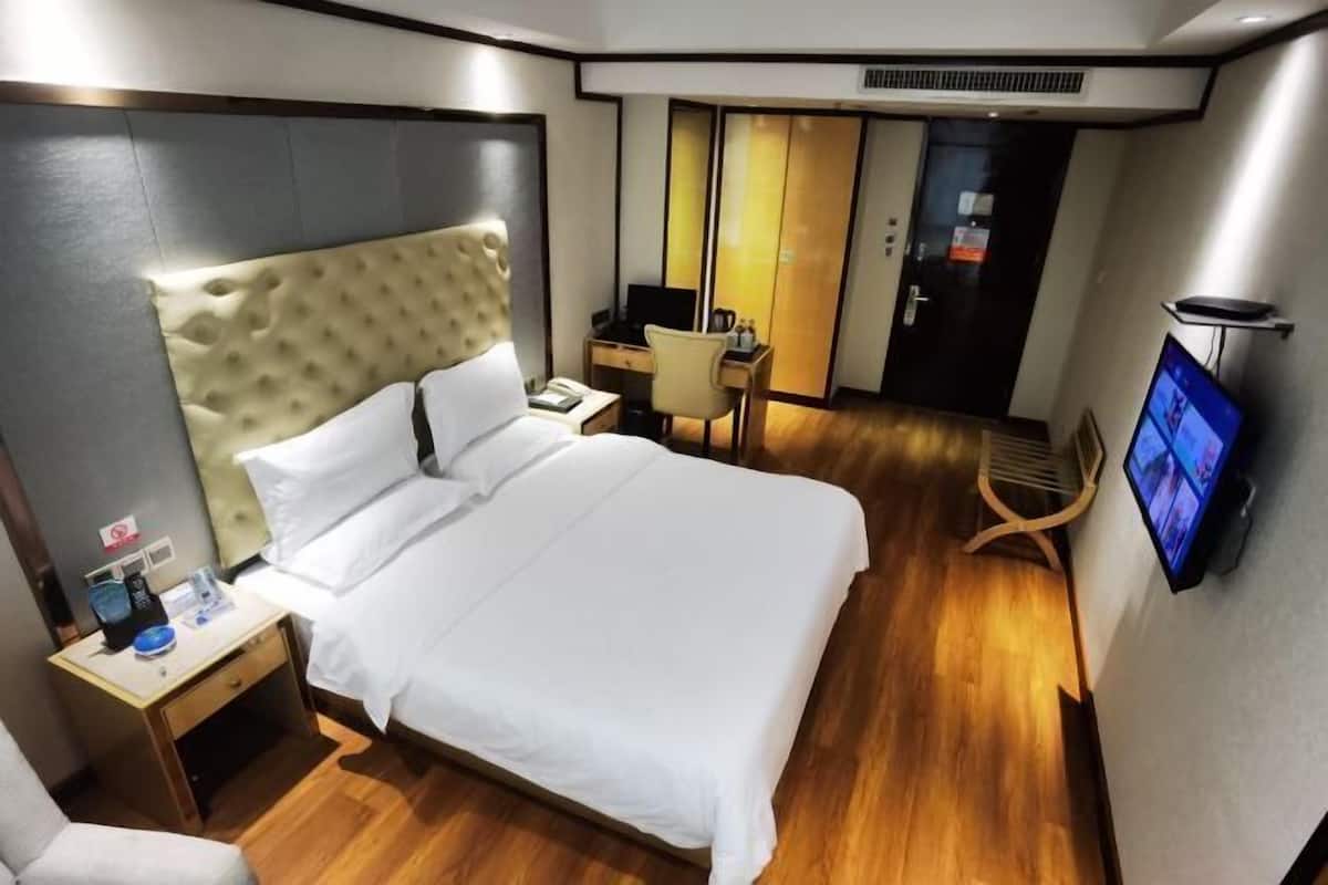 Quarto de hotel com uma cama grande, uma escrivaninha, uma cadeira, uma televisão e um guarda-roupa.