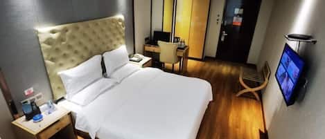 A hotel room with a large bed, a desk, a chair, a TV, and a wardrobe.