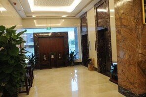 A hotel lobby with a marble reception desk, a large wooden door, and potted plants. - Zhao He Hotel (Nanning)