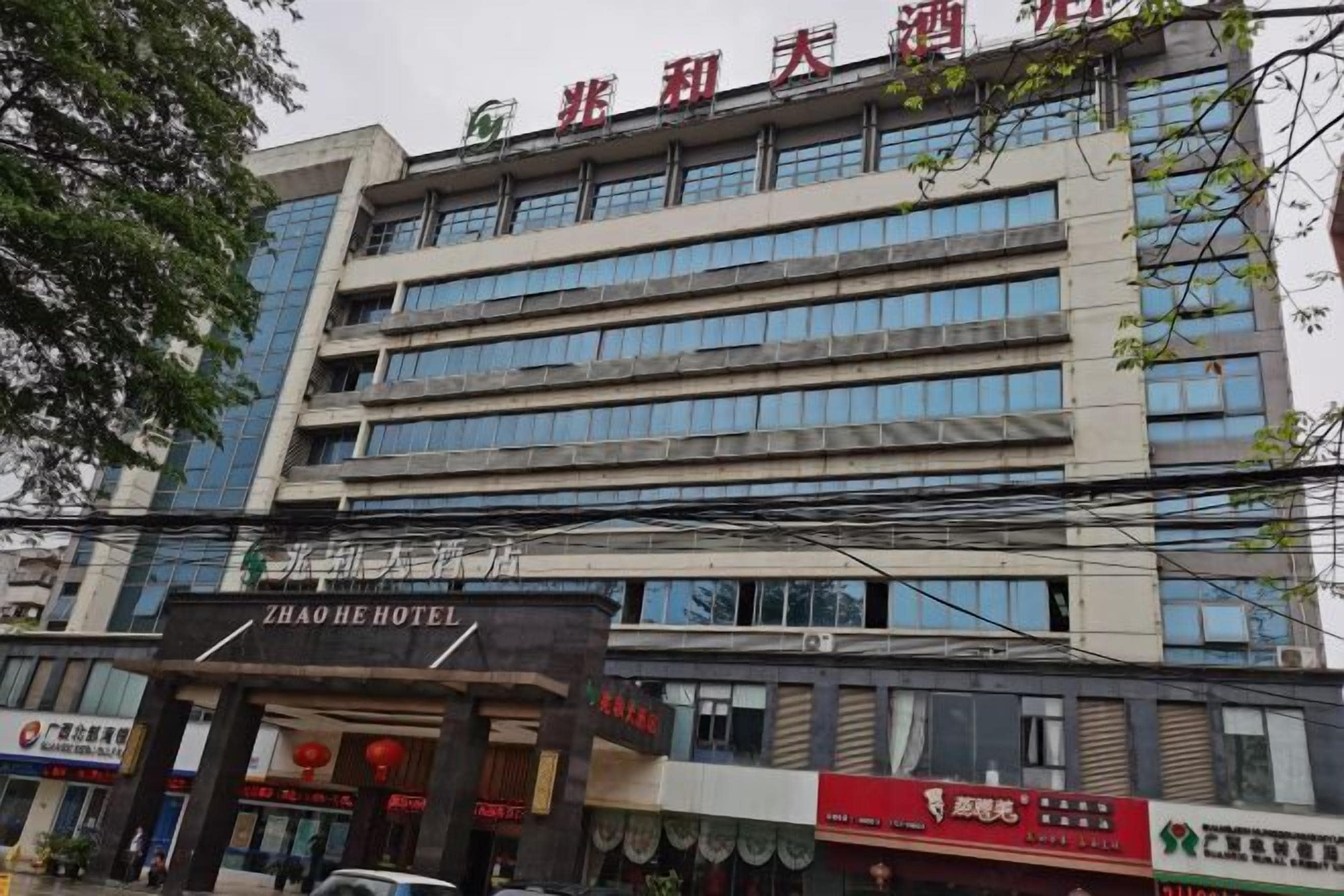 Un edificio de hotel de varios pisos con fachada moderna, que presenta grandes ventanales y un letrero llamativo del HOTEL ZHAO HE.