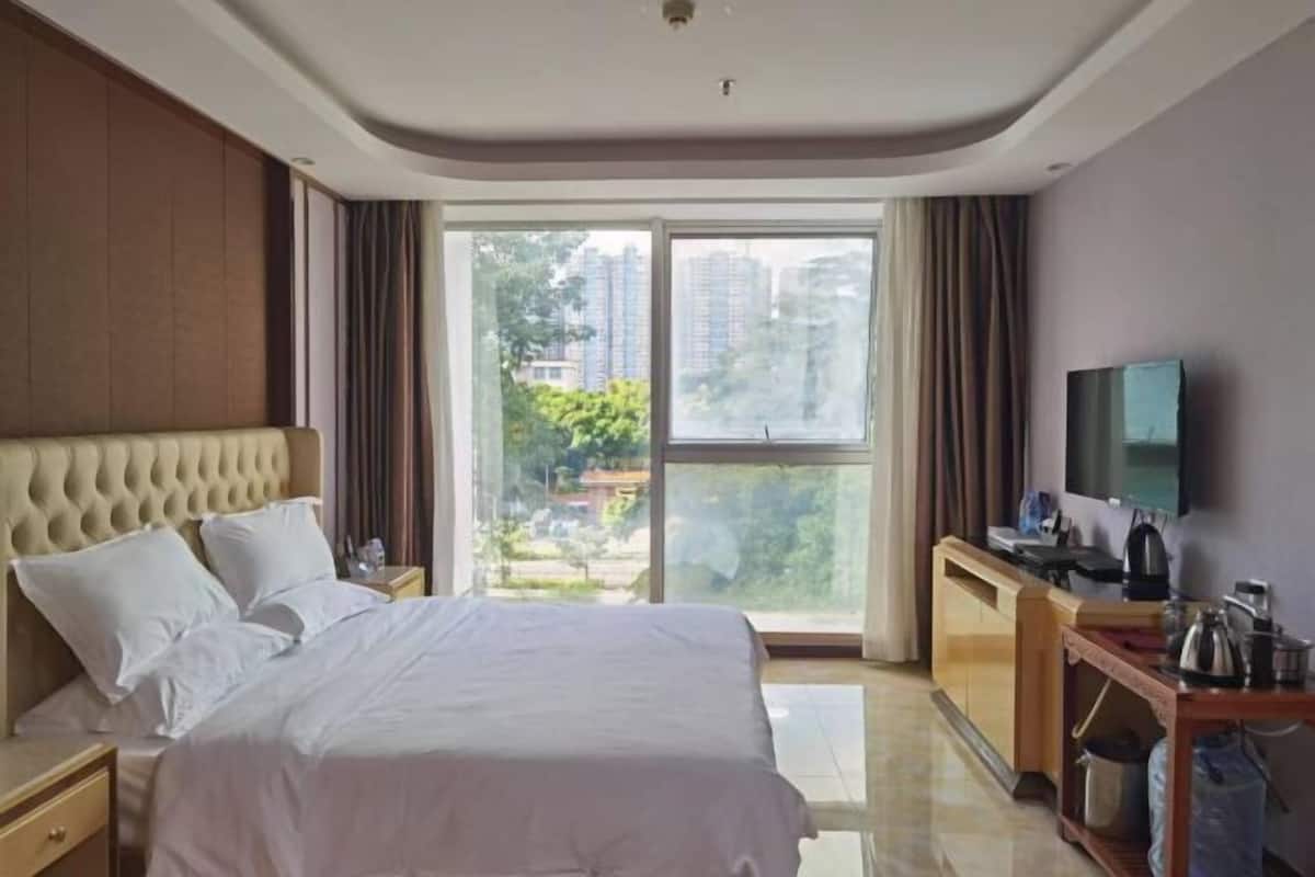 Quarto de hotel com uma cama grande, uma escrivaninha e televisão de tela plana, e vista da cidade através de amplas janelas.