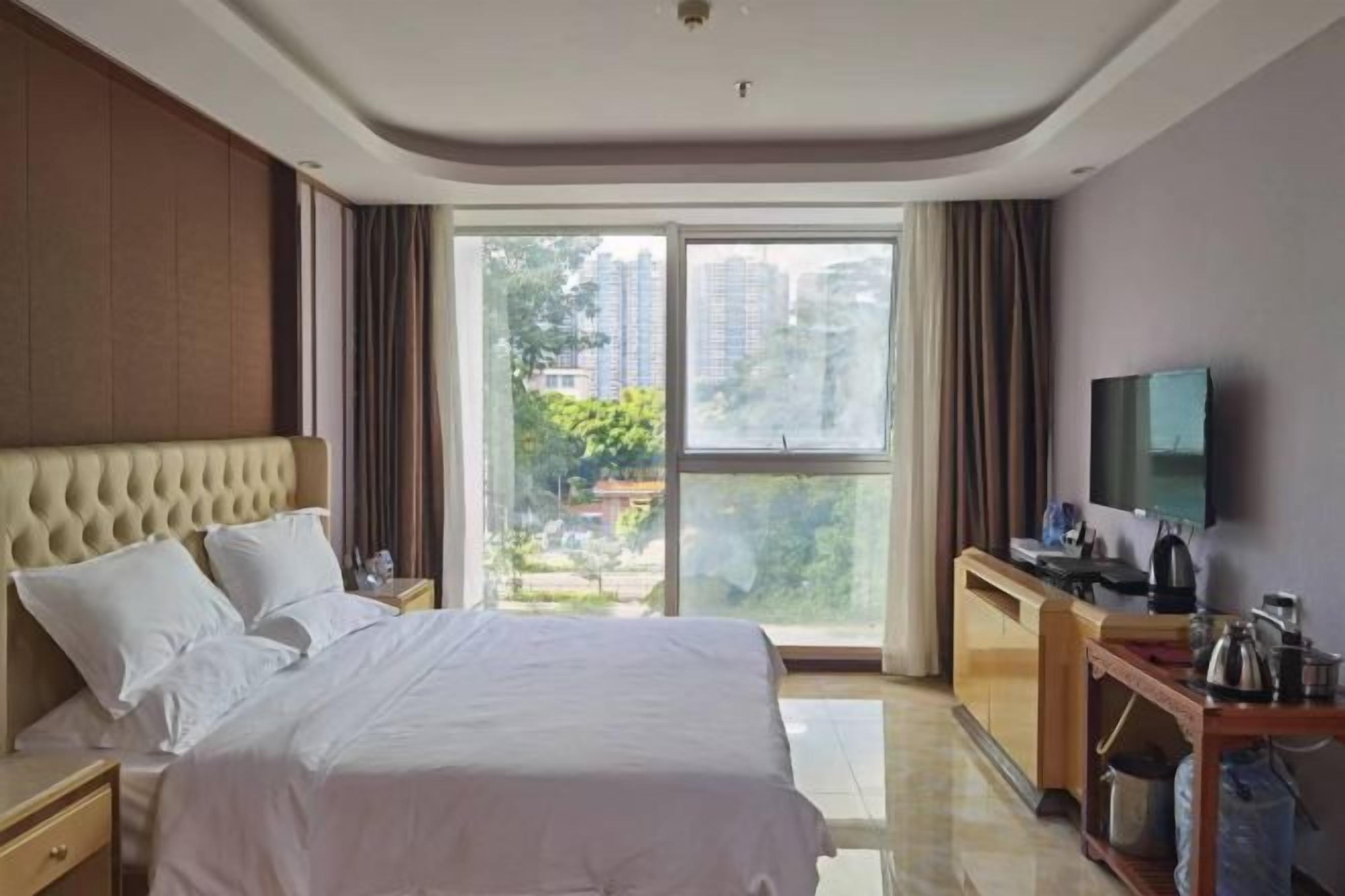 A hotel room with a large bed, a desk with a flat-screen TV, a window with a city view, and a sliding door to the balcony.