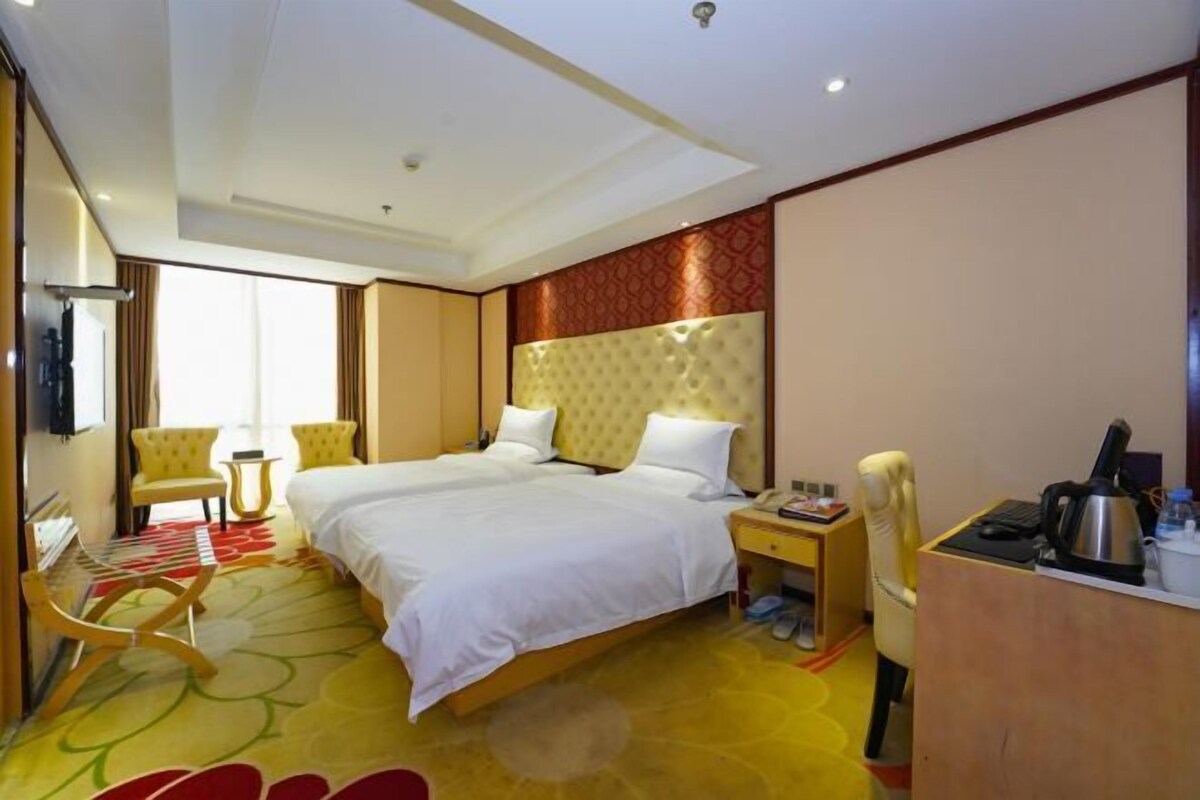 A hotel room with two beds, a desk, a chair, and a television.