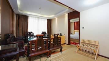 Habitación de hotel con una mesa de comedor de madera, dos sillas de madera, un pequeño banco de madera, una cama con cabecera roja y una mesita de noche con una lámpara.