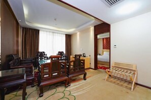 A hotel room with a wooden dining table, two wooden chairs, a small wooden bench, a bed with a red headboard, and a nightstand with a lamp. - Zhao He Hotel (Nanning)