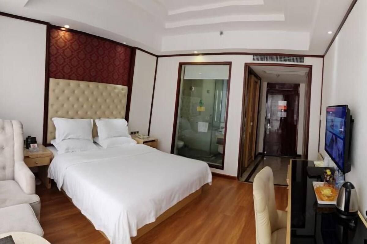A hotel room with a large bed, a desk with a television, and a seating area.