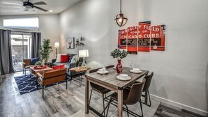 A modern living room with a dining area, featuring a large window, a ceiling fan, and a red Chicago Cubs sign on the wall. - ☺ Just Remodeled ☺ 3 Bed / 2 Bath Sparkling Townhouse with Patio! ☺ (Mesa)