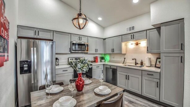 A modern kitchen with grey cabinets, stainless steel appliances, and a dining area with a wooden table set for two. - ☺ Just Remodeled ☺ 3 Bed / 2 Bath Sparkling Townhouse with Patio!   ☺ (Mesa)