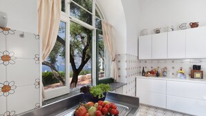 A kitchen with a sink, a window with curtains, and a view of trees and a body of water.