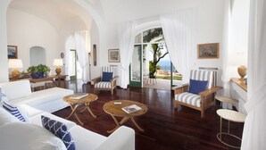 A spacious living room with a view of the sea, featuring a sofa, armchairs, and a coffee table.
