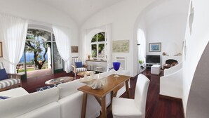 A spacious living area with a wooden dining table, white sofas, and a view of the outdoors.