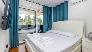 A modern bedroom with a bed, a bedside table, a TV, and a window with curtains. - Modern holiday house JASMINKA (Malinska)