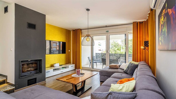 A modern living room with a grey sofa set, a fireplace, a flat-screen TV, and a dining area with a wooden table. - Modern holiday house JASMINKA (Malinska)