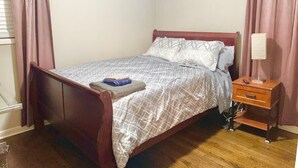 Un llit individual amb estructura de fusta, una tauleta de nit amb una làmpada i una finestra amb cortines.
