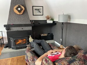 A cozy living room with a fireplace, a sofa, a lamp, and a framed picture on the wall. - Quaint Ski Chalet 5 Minutes to Mt Orford (Orford)