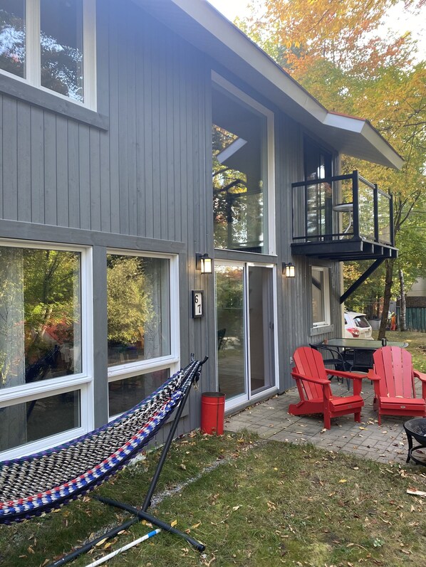 A modern house with large windows, a hammock, and red Adirondack chairs in the backyard. - Quaint Ski Chalet 5 Minutes to Mt Orford (Orford)