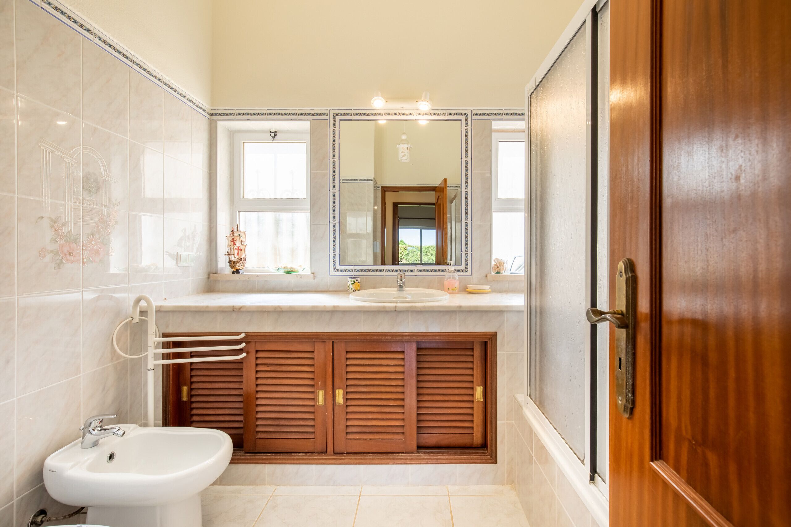 A bathroom with a marble vanity, a sink, a mirror, and wooden cabinets.