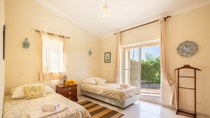 A hotel room with two beds, a wooden dresser, a small table with a lamp, and a view of the outdoors through a sliding glass door. - Villa Maren, quiet residential area, private pool (Lagos)