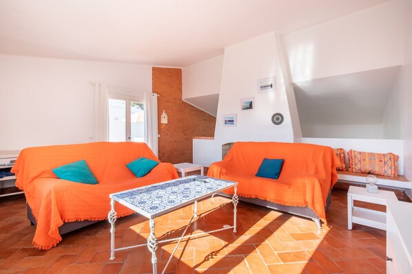 A bright living room with two orange sofas, a patterned coffee table, and a white bench.