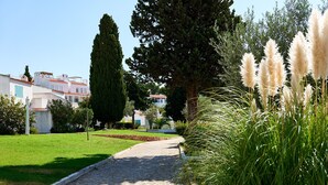 Uma passagem de paralelepípedos serpenteia por um jardim bem cuidado, com árvores altas e grama-de-pampa.