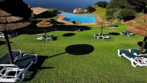 Área de piscina com espreguiçadeiras e guarda-sóis, rodeada por vegetação e com vista para o mar.