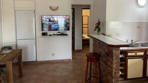 Ett kök med ett kylskåp, en tv som är monterad på väggen, ett matbord i trä och en köksbänk med en diskho.