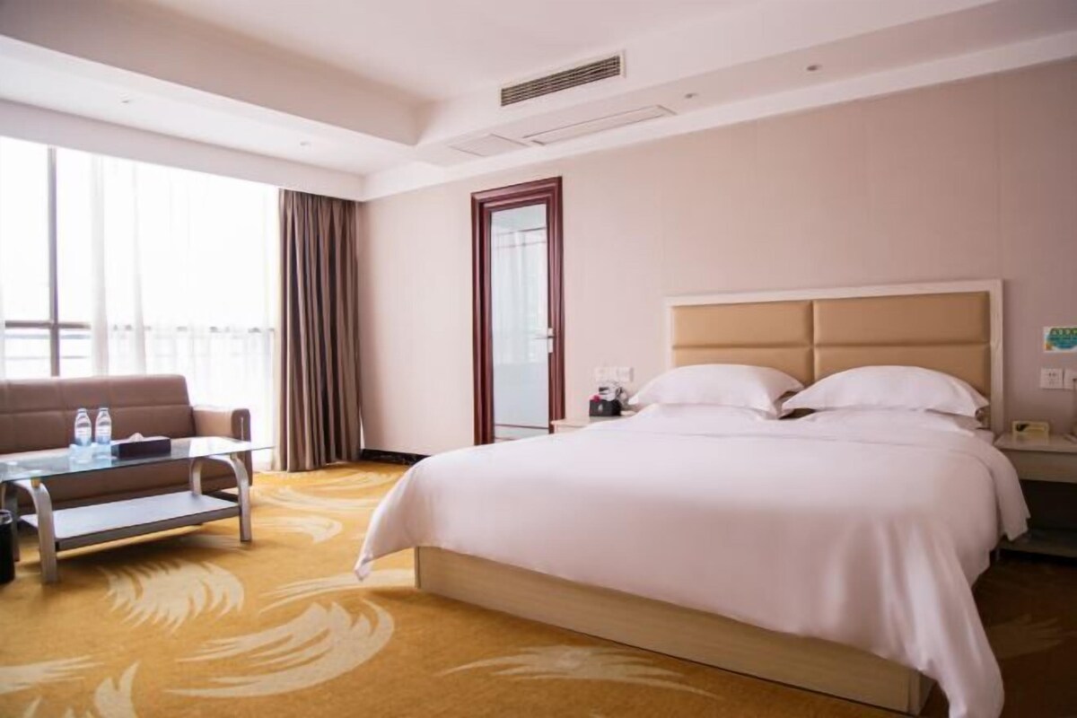 Een hotelkamer met een bed, een bank, een glazen salontafel en uitzicht op het landschap.