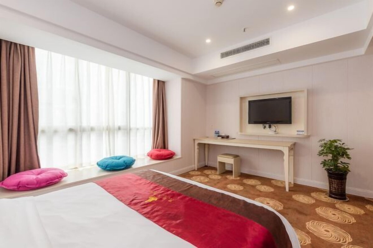 Een hotelkamer met een bed, een bureau, een televisie en een raam met gordijnen.