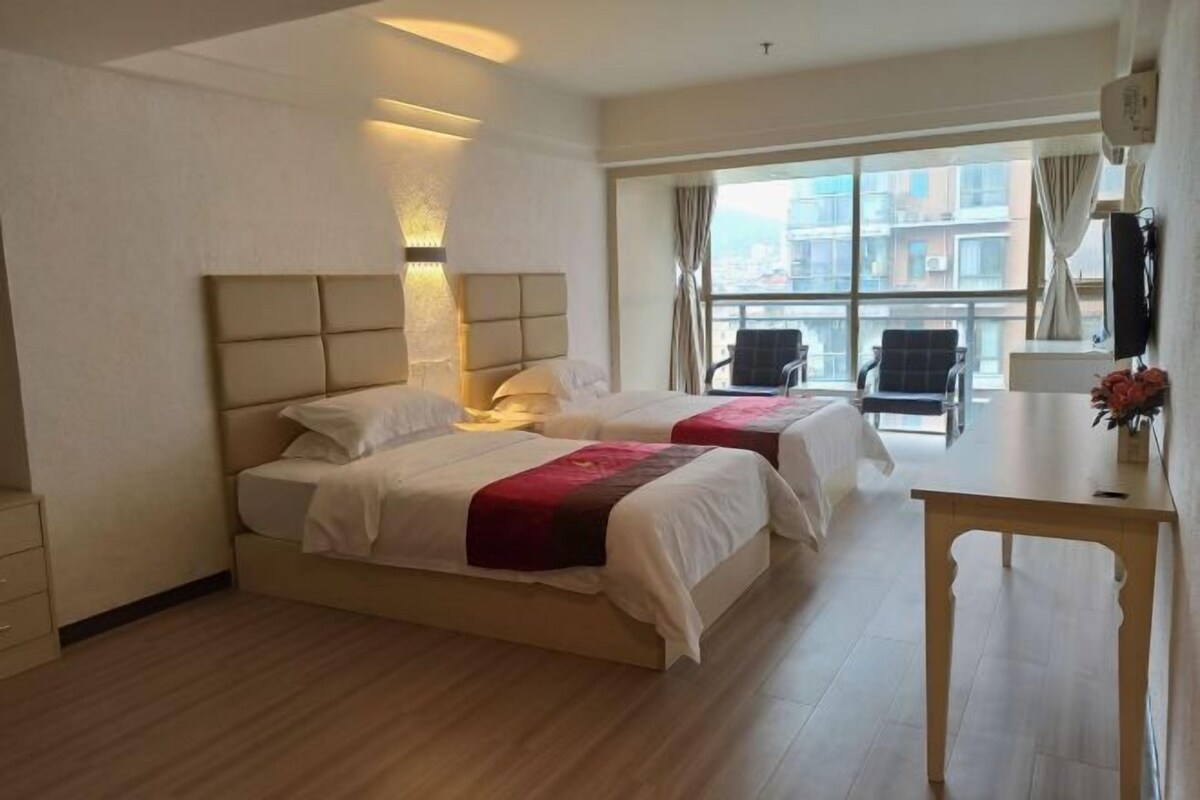 Een hotelkamer met twee bedden, een bureau en een groot raam met uitzicht op de stad.