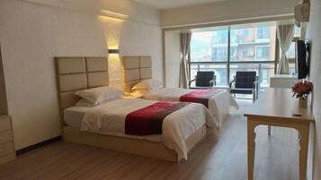 Habitación de hotel con dos camas, un escritorio y un ventanal con vistas a la ciudad.