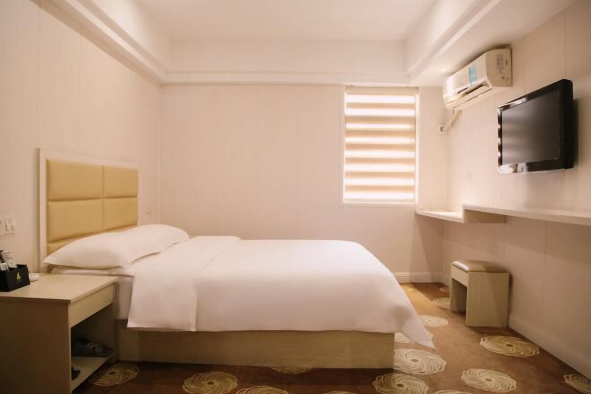 Een hotelkamer met een bed, nachtkastje en een aan de muur bevestigde televisie.