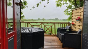 A covered outdoor seating area with a wooden deck, a red door, and a view of a green field. - 1 bedroom nice (sta)caravan in Gommenec h (Gommenec h)