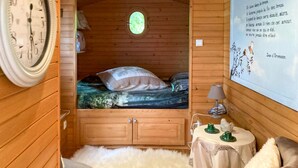 A cozy wooden cabin room with a bed, a small table with a lamp, and a wall clock. - 1 bedroom nice (sta)caravan in Gommenec h (Gommenec h)