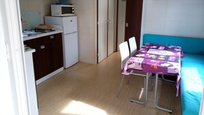 Ett kompakt kök med mikrovågsugn, spishäll och skåp. Här finns ett matbord med stolar och en blå soffa.