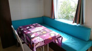 Ett litet rum med en turkosfärgad soffa, ett bord med en färgglad duk och ett fönster med gardiner.