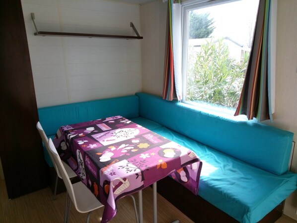 A small room with a teal sofa, a table with a colorful tablecloth, and a window with curtains.