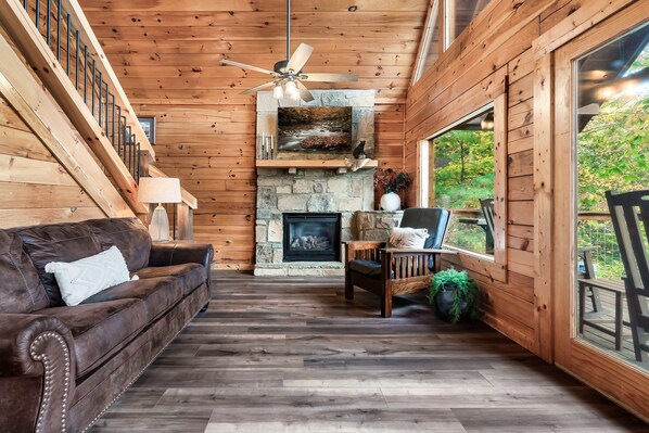 Ein gemütliches Blockhaus-Interieur mit Kamin aus Naturstein, Holzwänden, einer Ledersofa und einem Essbereich.