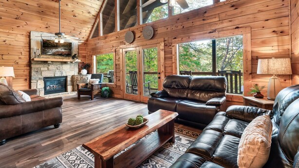 Ein geräumiges Wohnzimmer mit Kamin aus Stein, Ledersofas und einer großen Holzbalkendecke.
